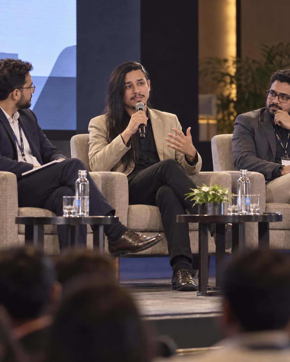 Wendeel Marinho participando de um painel, sentado entre dois debatedores e falando ao microfone.