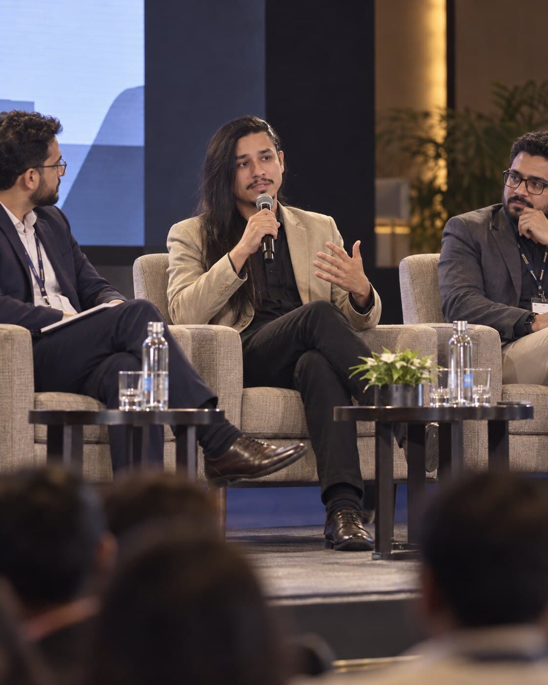 Wendeel Marinho participando de um painel, sentado entre dois debatedores e falando ao microfone.